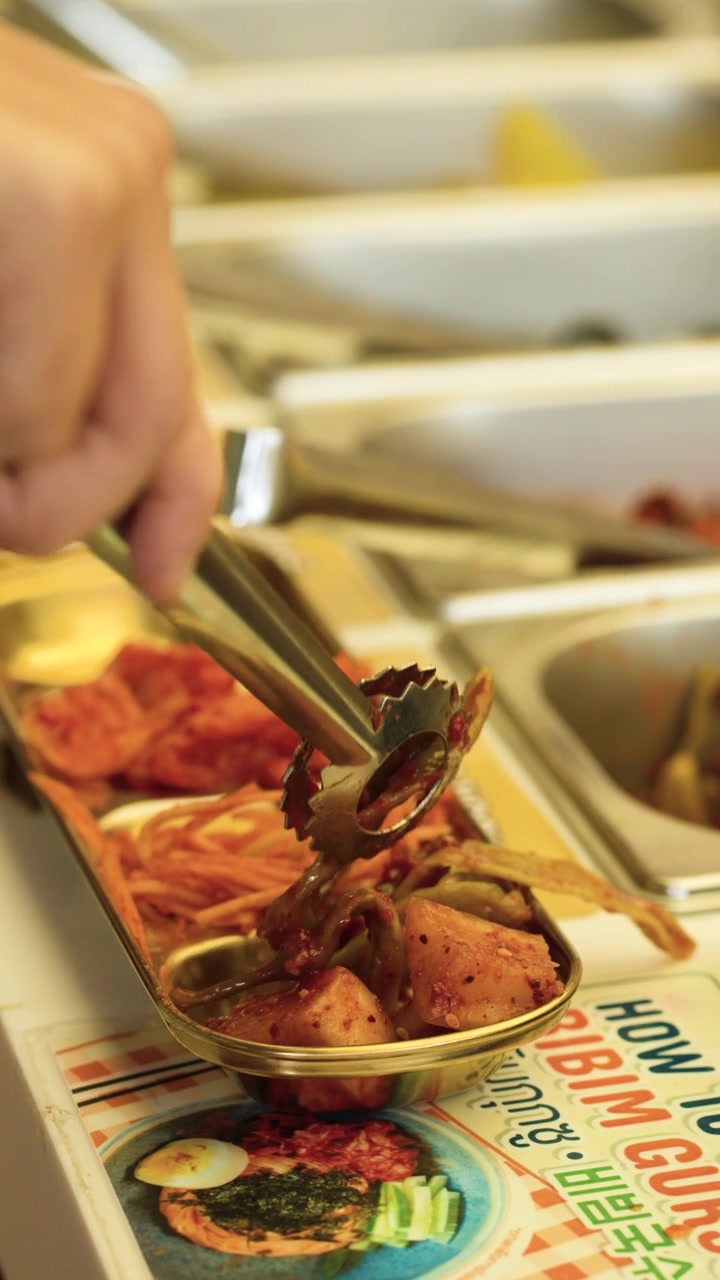 Nærbillede af en hånd, der bruger metaltang til at vælge tilbehør ved en buffet.