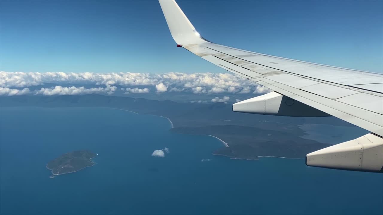 View from an airplane cruising over the coast of North Queensland in Australia, with scalloped coastline, islands, blue sky and low clouds over the continent
