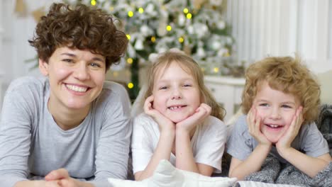 portrait of beautiful mother, little daughter and cute son lying together on bed and smiling at camera on christmas