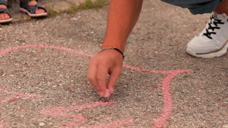 a father with his child draws on the ground a pink heart with chalk