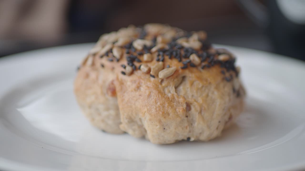 Hand Picks Up Seeded Bread Roll from White Plate