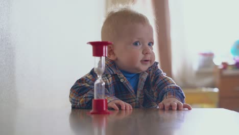 el bebé en camisa se para en la mesa y la mamá pone el vidrio de arena