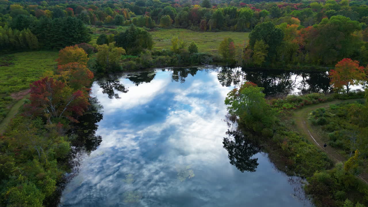 Aerial flyby shot of a stream of lake with greenery on either side of it during daytime in Massachusetts, USA. Reflection of sky on lake.