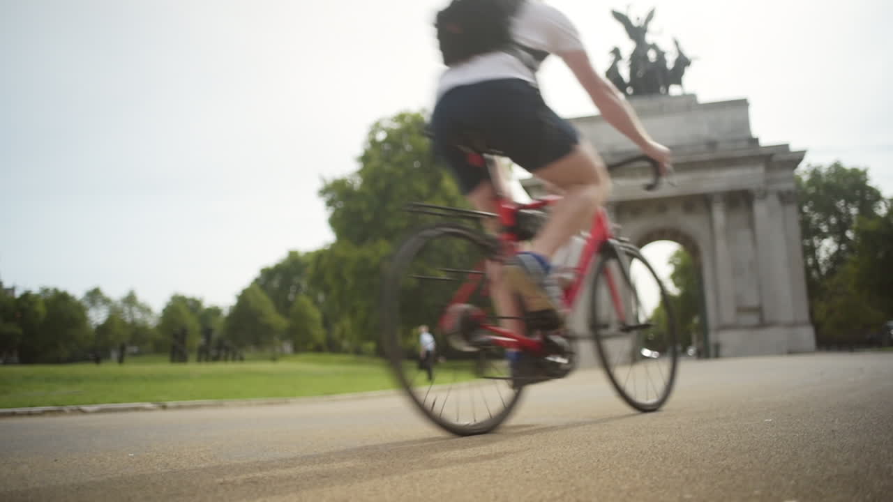 Cyclist with helmet and backpack rides bicycle through stone arch in park in London