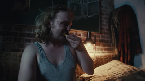 man eating and feeling sad in bedroom at night