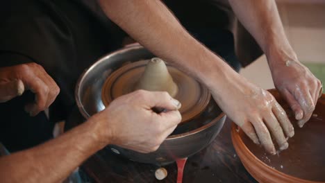 old experienced guy teach man how to use potter's wheel to create handmade clay product