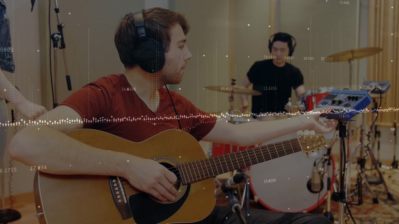 Seated guitarist reaching tuner to tune guitar while strumming in studio, waveform showing levels
