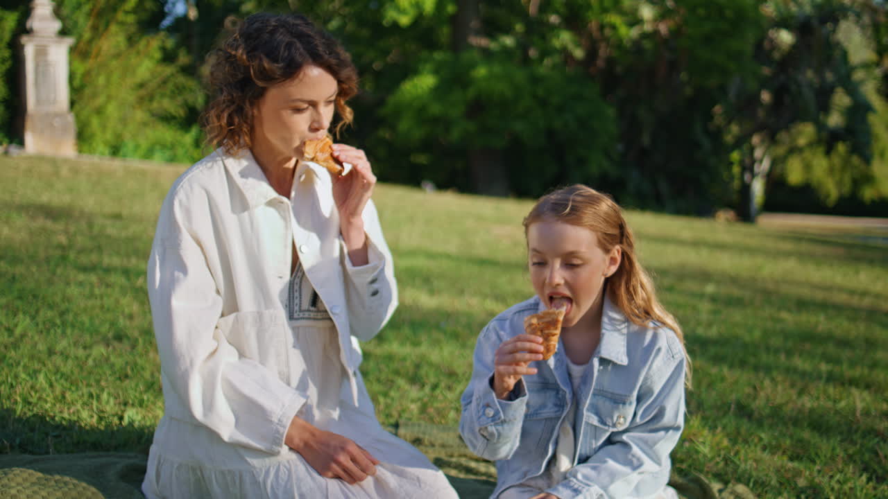 Happy kid sharing croissant with mom on family picnic. Mother child conversation