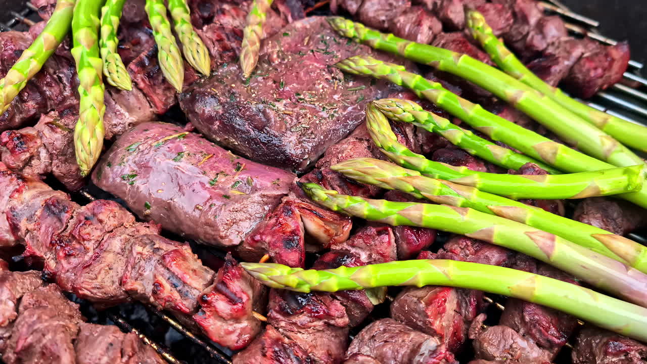 Juicy grilled beef steaks and skewers with fresh asparagus spears cooking on a barbecue at an outdoor picnic in Latvia
