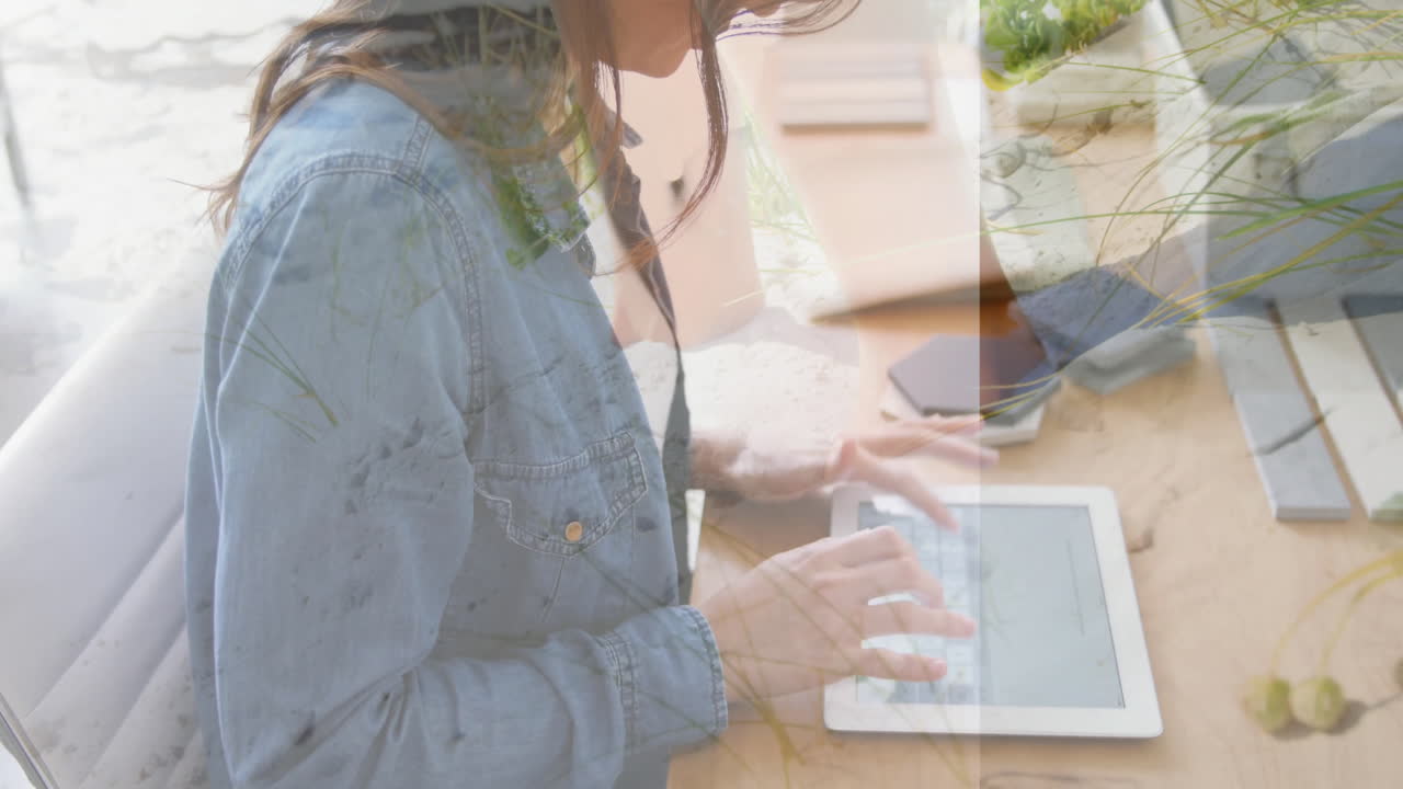 Using tablet at desk, woman with nature overlay animation in background