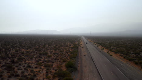 Luftaufnahme-Eines-Autos,-Das-Auf-Einer-Straße-Durch-Die-Mojave-Wüste-Fährt,-Mit-Dickem-Rauch-Am-Himmel-Von-Kalifornischen-Waldbränden
