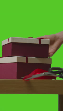 vertical video of man putting down pile of presents in gift wrapped boxes from table shot against green screen