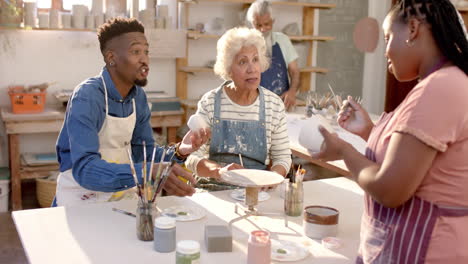 Happy-diverse-group-of-potters-glazing-clay-jugs-and-discussing-in-pottery-studio