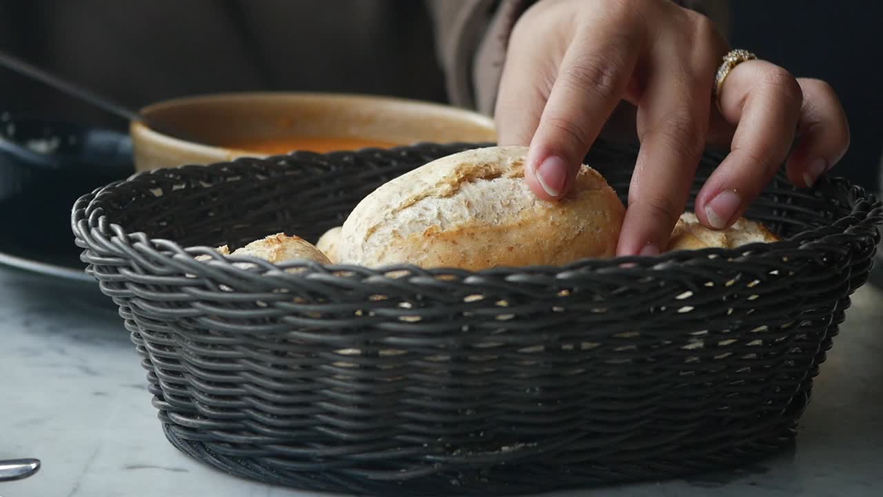 Hand Reaching for a Fresh Bread Roll from a Basket