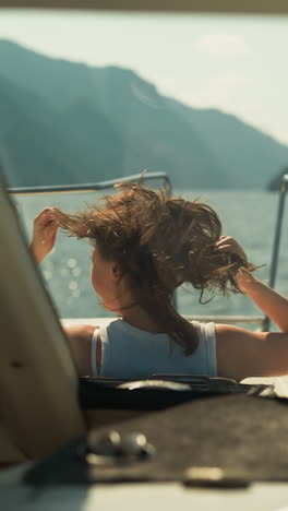 positive female sits on motorboat deck at windy seaside in sunny weather. young woman sails yacht in ocean on exotic vacation. tourist area viewing