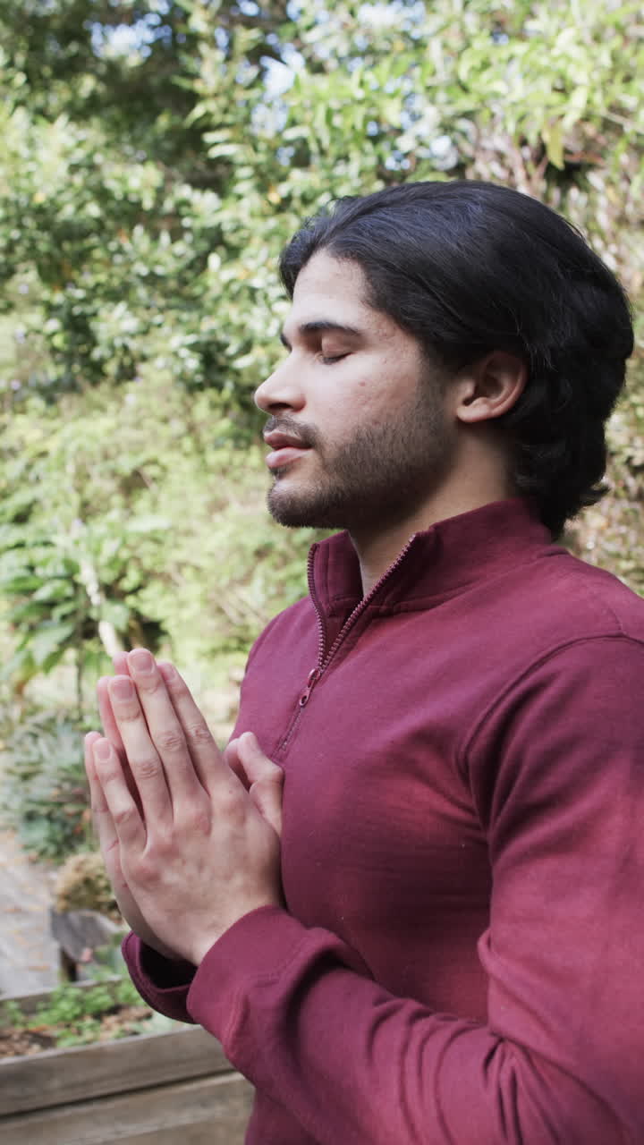 Vertical video of biracial man practicing yoga meditation on terrace in nature, slow motion