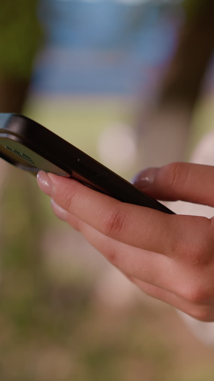primer plano de la mano del individuo deslizándose sobre la pantalla del teléfono inteligente, involucrado en la interacción, el fondo natural al aire libre está suavemente borroso, mientras que los toques de vegetación y una figura indistinta en la distancia