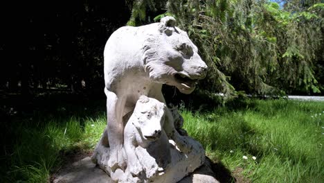 eine statue einer löwin und ihres löwenjungen in weißem stein in einem grünen garten