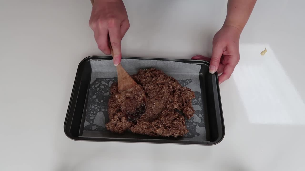 Putting caramel slice ingredients into a baking tray and spreading it