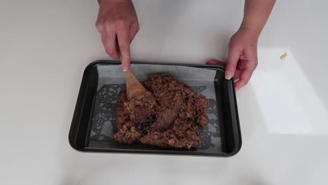 putting caramel slice ingredients into a baking tray and spreading it