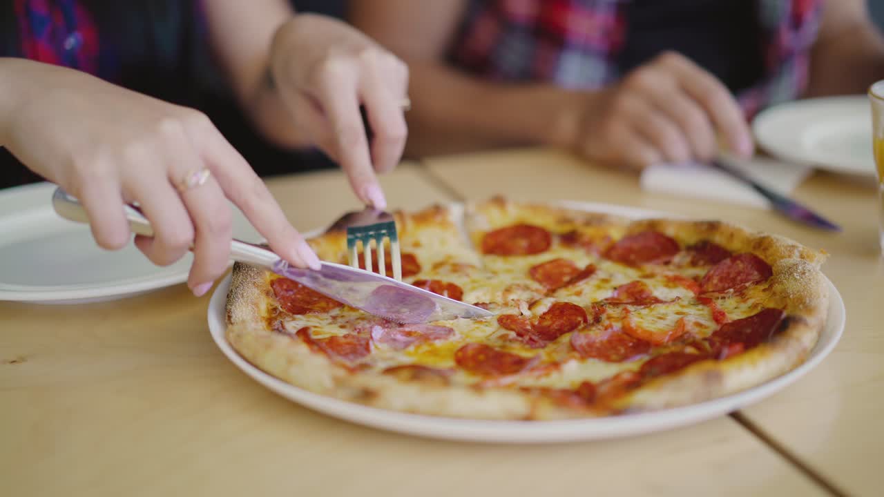 여자의 손은 소시지와 치즈로 뜨거운 피자를 잘라서 한 조각을 사랑스러운 접시에 넣습니다.