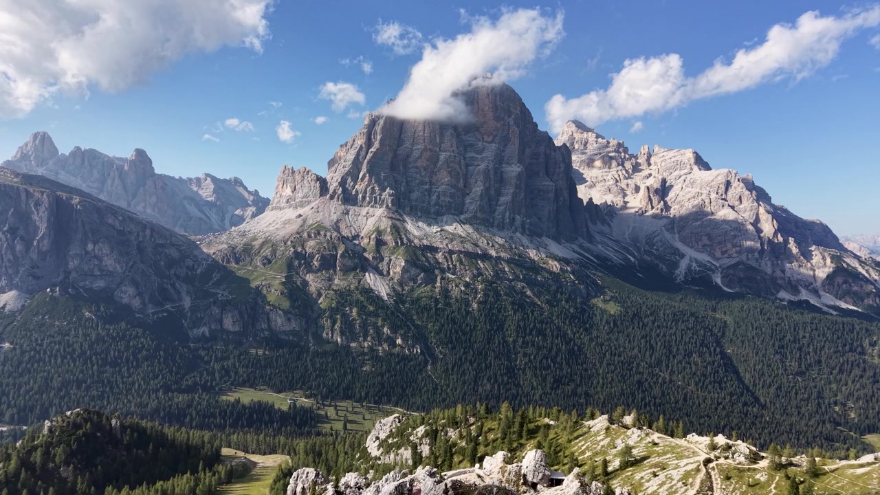 Vista cinematografica con drone della Tofana di Rozes filmata dalla zona delle Cinque Torri, che mostra l'iconico massiccio calcareo sotto un cielo azzurro nelle Dolomiti, Italia.