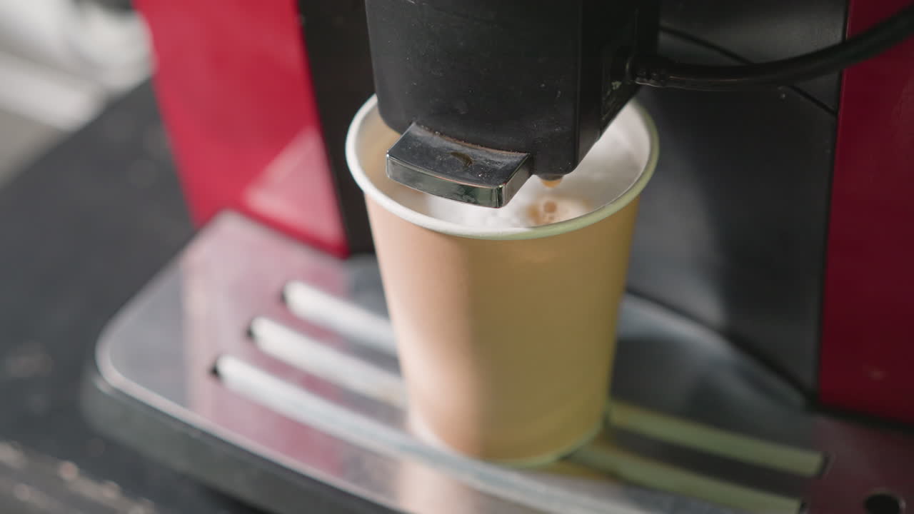 Close-up of coffee machine dispensing hot coffee into disposable paper cup, with focus on the coffee pouring and steam rising, capturing the brewing process in a kitchen setting