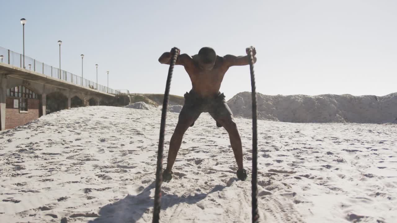 hombre afroamericano ejercitándose con cuerdas de lucha al aire libre en la playa