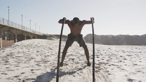 uomo afroamericano che si esercita con corde da combattimento all'aperto sulla spiaggia