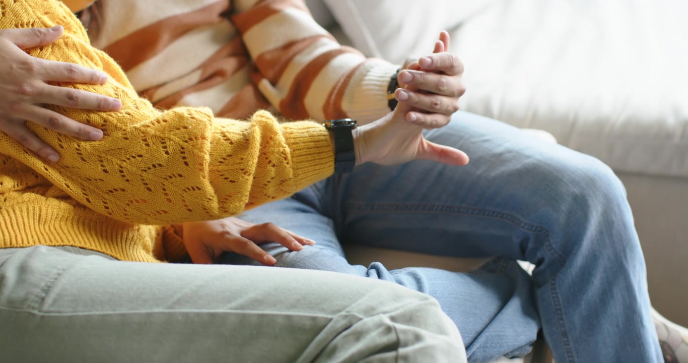Coppia afroamericana seduta sul divano, la donna con un maglione giallo estende il polso per mostrare un orologio scuro.