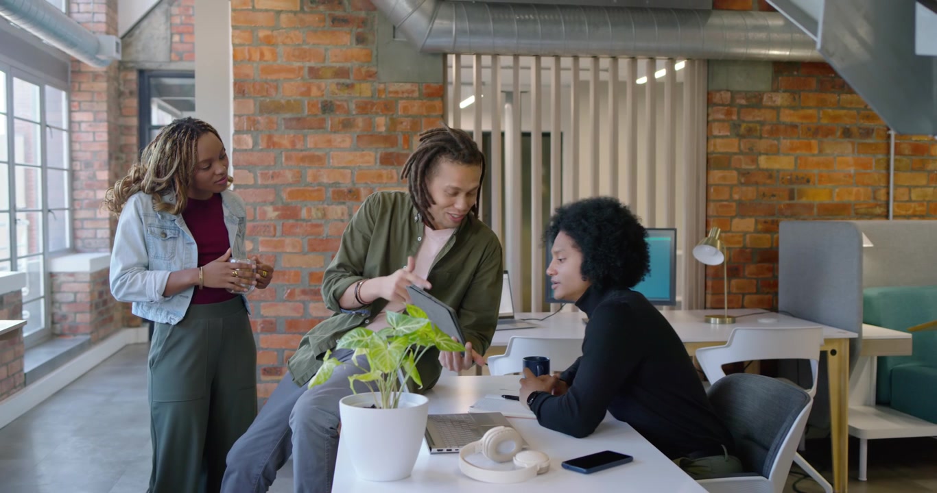 African American coworkers reviewing project after man pointing tablet, seated woman tapping screen