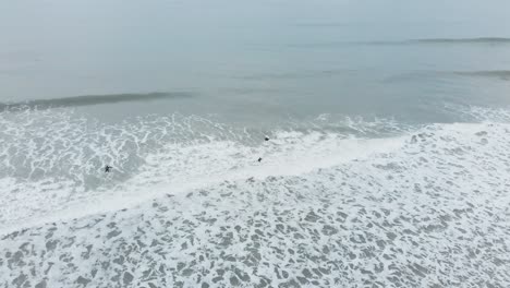 three people paddling and body surfing in foaming white water, aerial