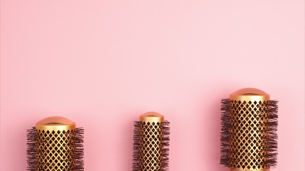 Stop motion animation of professional gold round hair brushes for styling at the bottom of the image template with copy space on pink background. Hairdresser salon equipment concept, premium set