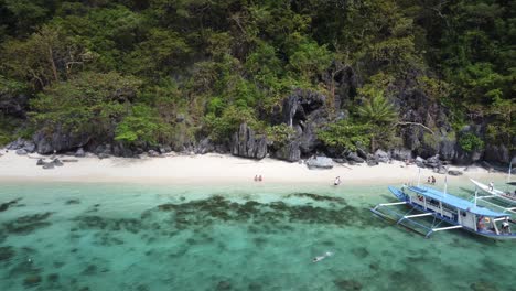 holidaymaker tourists of two island hopping tour boats snorkeling and relaxing on white sand of paradise beach on cadlao island - el nido amid tropical scenery