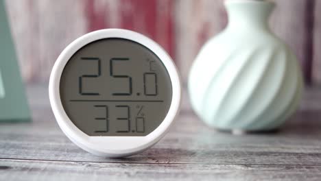 higrómetro digital y termómetro con jarrón en mesa de madera