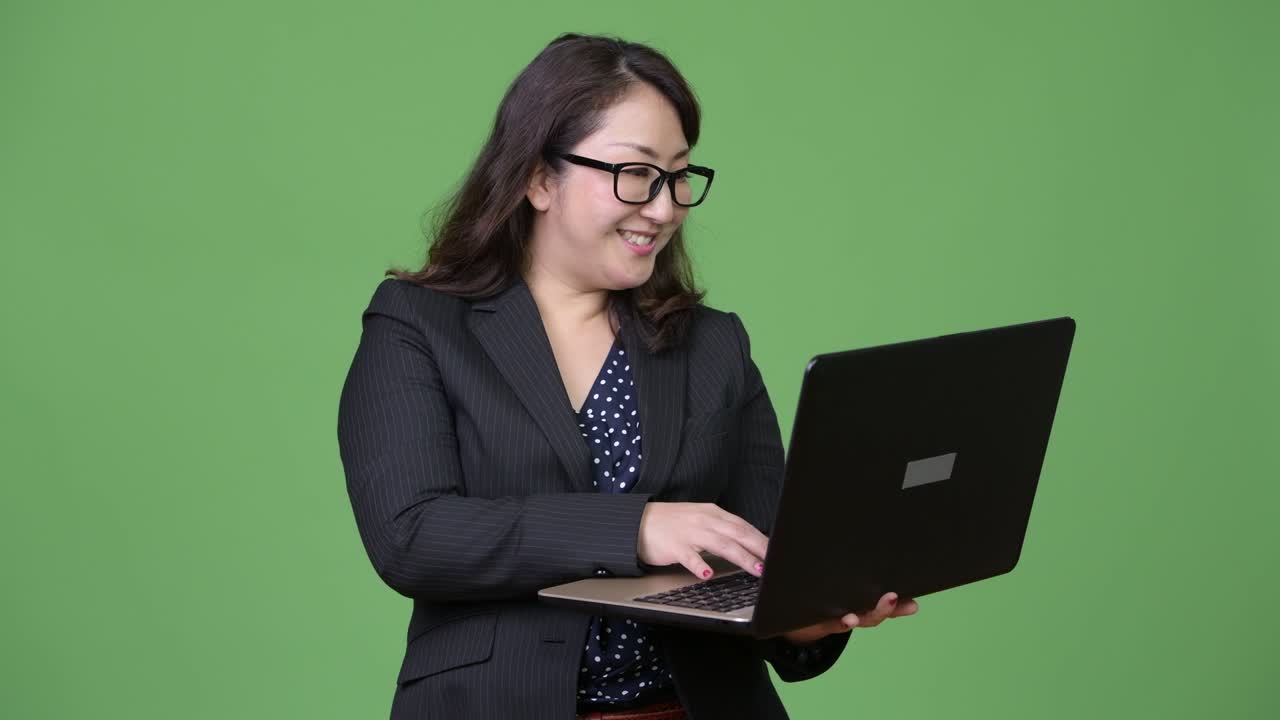 una hermosa mujer de negocios asiática madura usando una computadora portátil contra un fondo verde