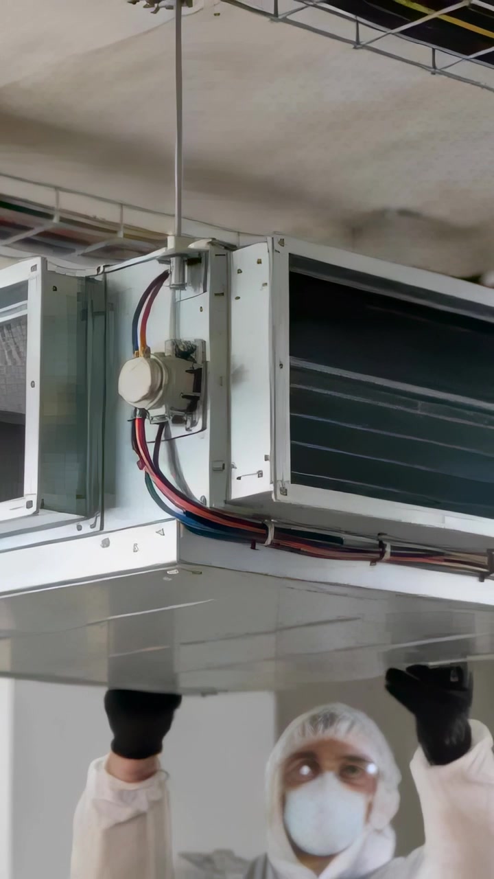Vertical video: Inspecting tech in coverall reaching under ceiling unit, adjusting motor and cables