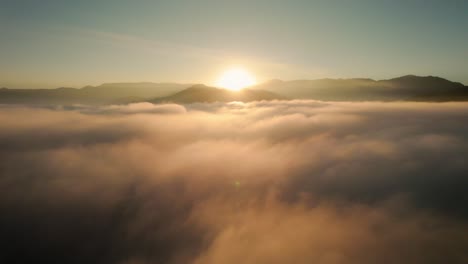 drone aerial view flying above beautiful heavenly clouds during epic warm sunrise with mountains in background