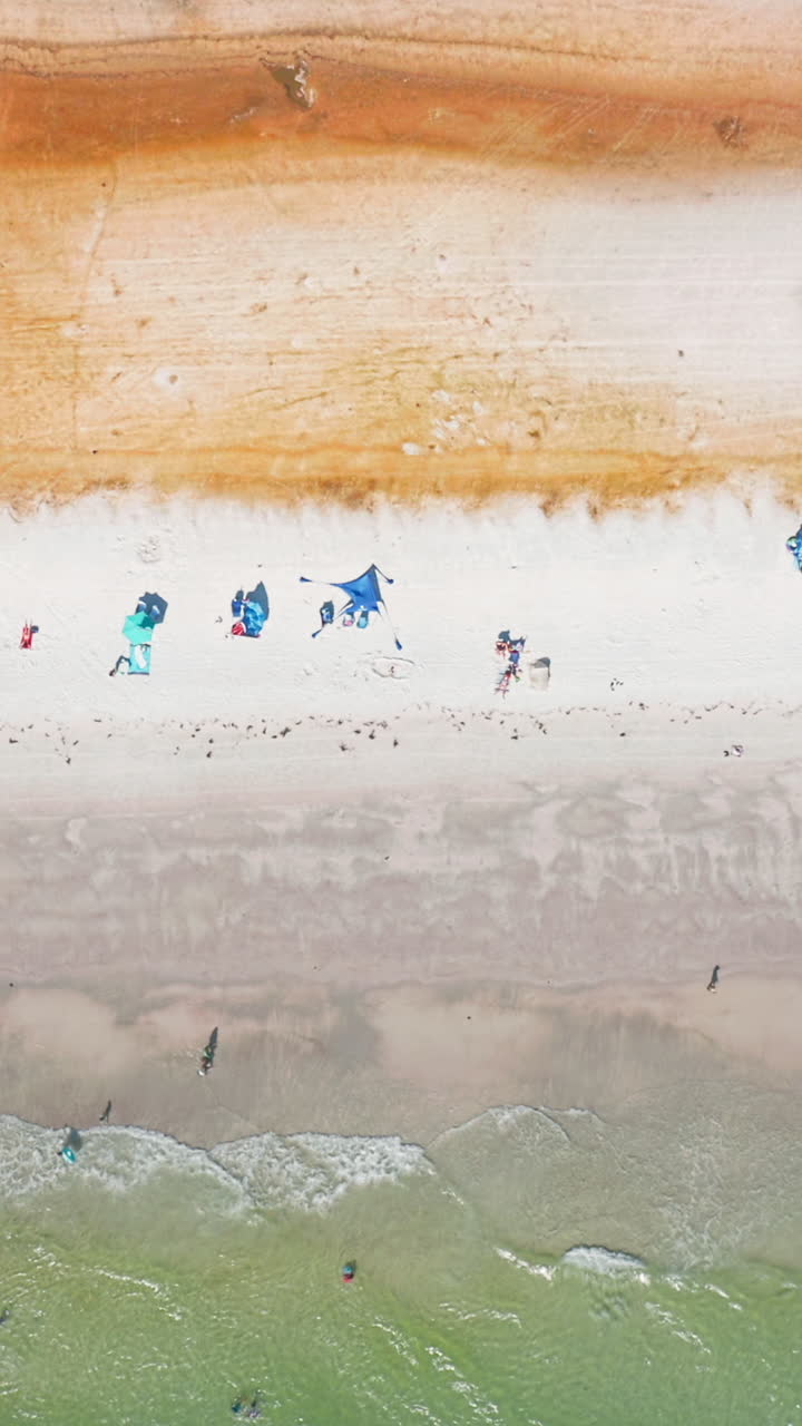 Bright beach tents dot the pristine white sand where turquoise waters roll ashore, framed by a strip of golden dunes that adds vivid contrast to the beachscape