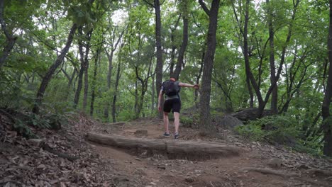 Side-view-of-the-male-hiker-walking-up-the-hill-following-the-trail-path-in-the-woods