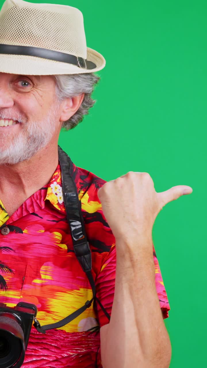 Uomo sorridente con camicia hawaiana e cappello che indica con la macchina fotografica su schermo verde