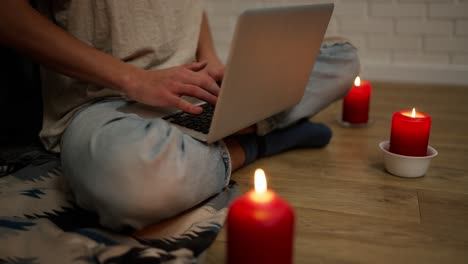 cropped footage of a woman working on modern laptop while sitting in a cozy room around candles