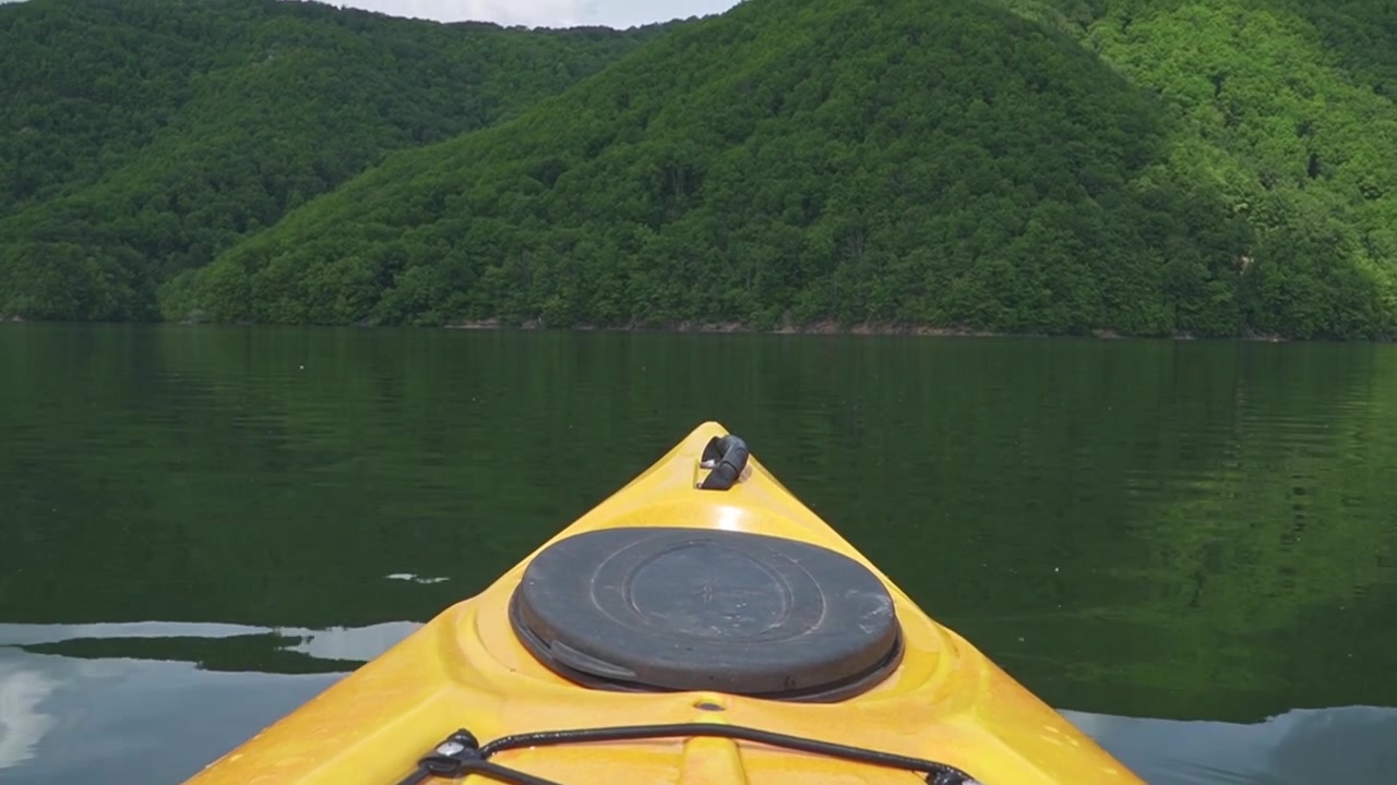 La prua di un kayak giallo fende le acque calme e riflettenti di un lago, circondato da rigogliose colline verdi. Ideale per contenuti di avventura o temi di stile di vita all'aperto.