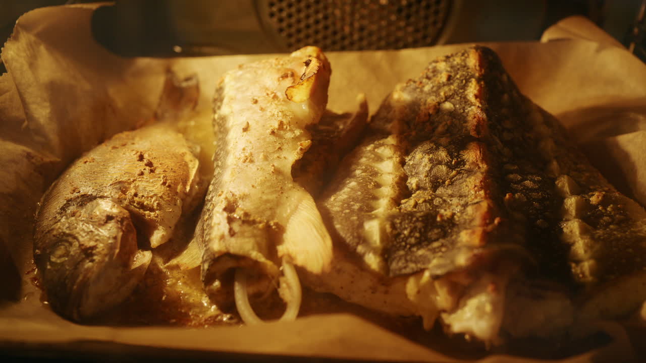 Fresh fish pieces roasting in the oven on a tray, golden surface and steam visible