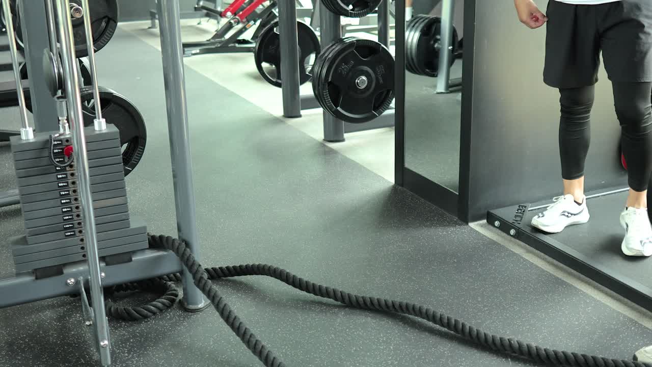 Two people prepare for a battle rope workout in a modern, brightly lit gym