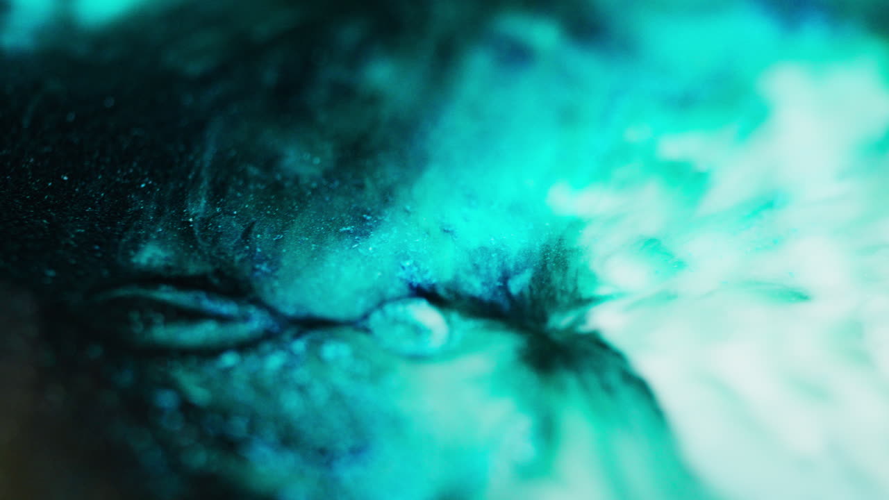 Macro video of fluid blue, green, and black ink moving and blending in smooth abstract patterns