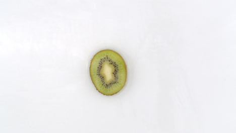 Sobre-Un-Fondo-Blanco,-Una-Rodaja-De-Kiwi-Cae-Al-Agua-Con-Un-Chapoteo.