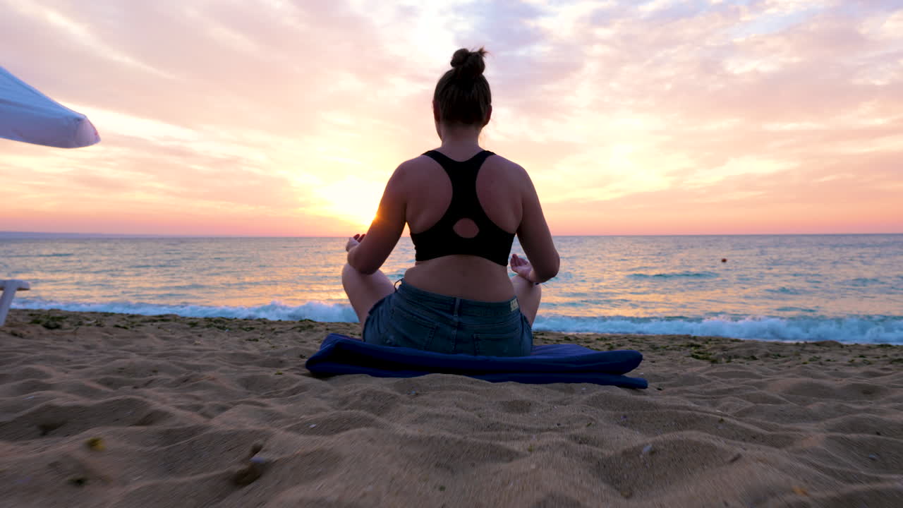 Woman sits on the beach practicing yoga at the sunrise
