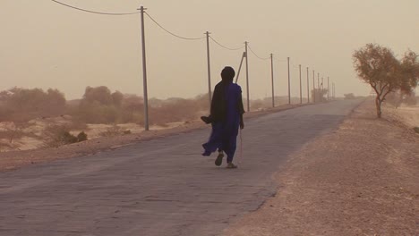 a touareg person walks down a road through the sahara desert in mali