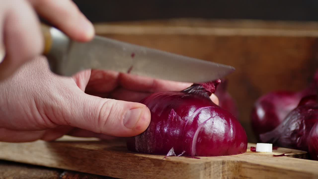 manos masculinas cortando cebolla roja en una tabla de cortar de madera.